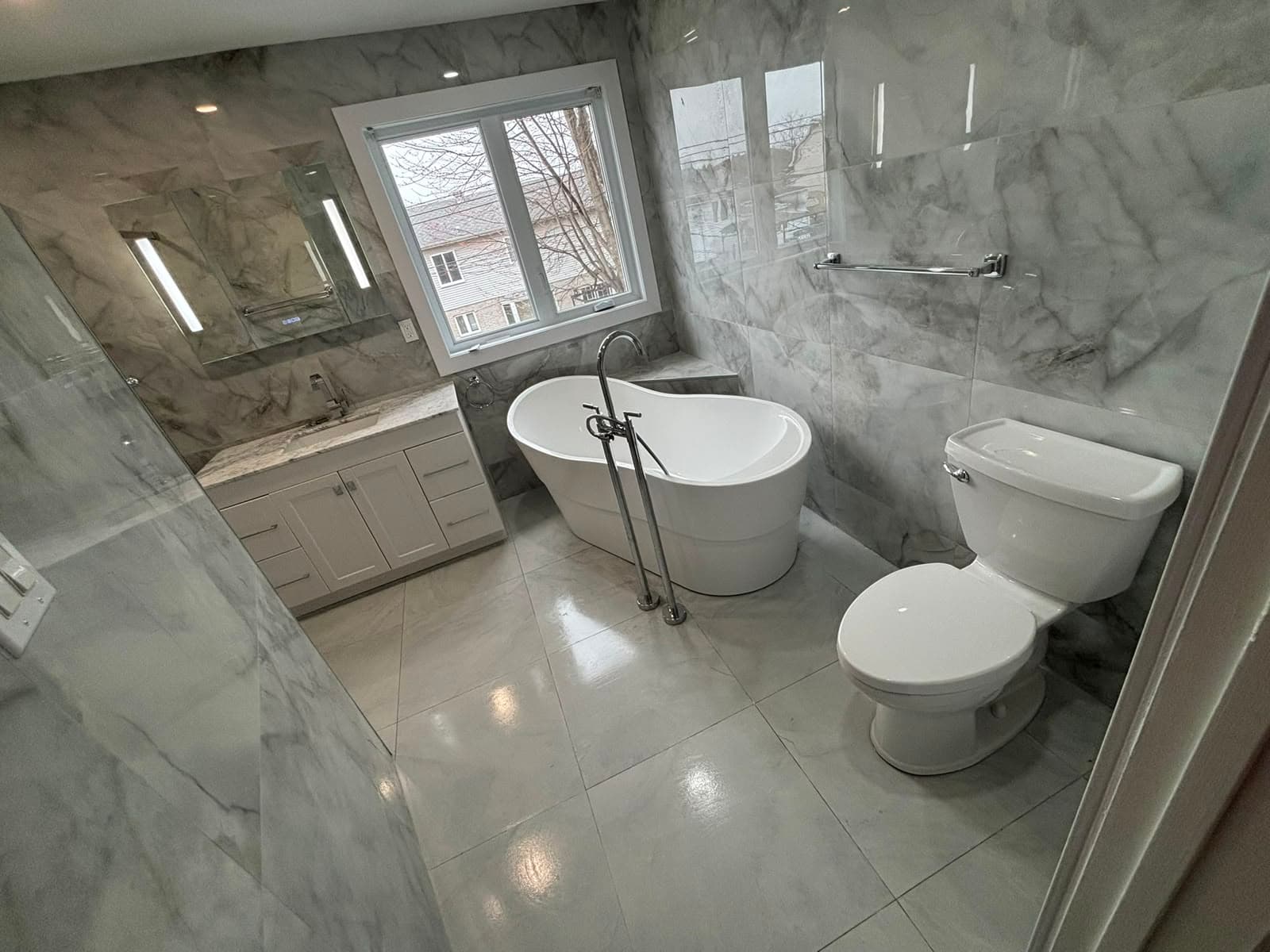 Salle de bain avec bain autoportant, douche en verre et céramique effet marbre
